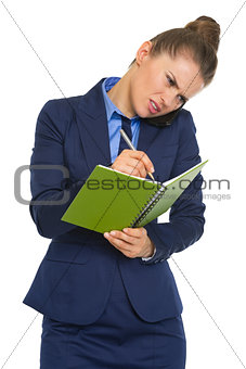 Concerned business woman talking mobile phone and writing in not
