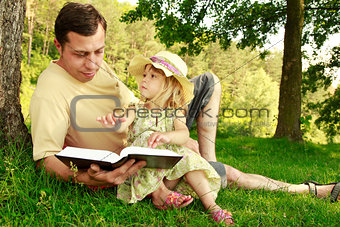 young father with his little daughter reads the Bible 