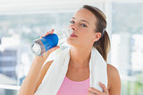 Woman with towel drinking water in gym