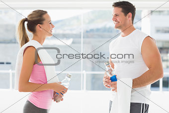 Fit couple holding water bottles and towels in exercise room