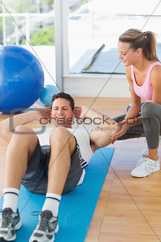Female trainer looking at young man do abdominal crunches