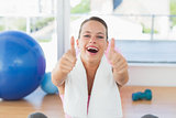 Woman with towel gesturing thumbs up in gym