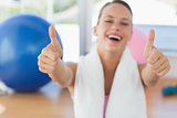 Woman with towel gesturing thumbs up in gym