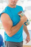 Mid section of a sporty man with dumbbell in gym