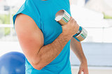 Mid section of a sporty man with dumbbell in gym