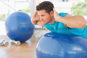 Young man exercising on fitness ball at a bright gym