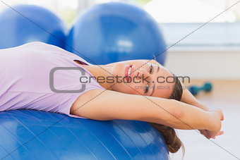 Smiling fit woman lying on exercise ball at gym