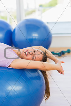 Smiling fit woman lying on exercise ball at gym