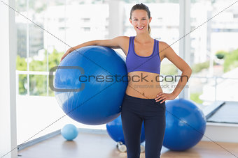 Smiling fit woman holding fitness ball in gym