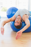 Happy fit man stretching on exercise ball at gym