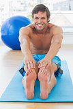 Sporty man stretching hands to legs in fitness studio