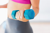 Mid section of a woman lifting dumbbell weight in gym