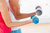 Mid section of a sporty young couple with dumbbells