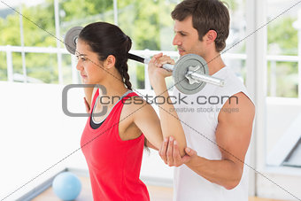 Male trainer helping fit woman to lift the barbell