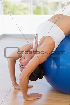 Fit woman stretching on exercise ball at gym