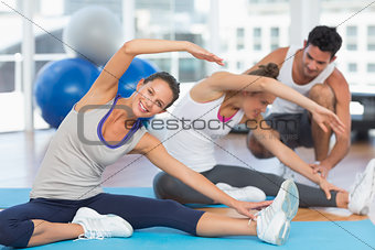 Women doing stretching exercises as trainer helps one