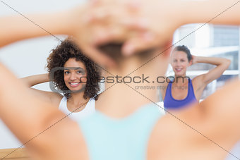 Smiling females with blurred trainer doing stretching exercises