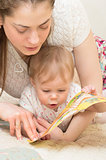 The mother reads the book to the baby.