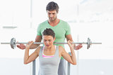 Trainer helping fit woman to lift barbell bench press