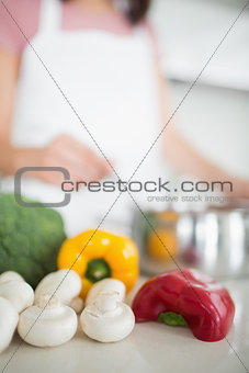 Vegetables with blurred woman preparing food in kitchen