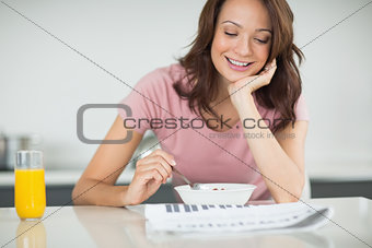Woman with a bowl of cereals reading newspaper in kitchen