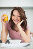 Woman with a bowl of cereals, orange juice and newspaper in kitchen