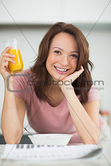 Woman with a bowl of cereals, orange juice and newspaper in kitchen