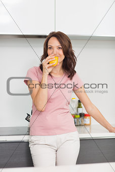 Smiling woman drinking orange juice in kitchen
