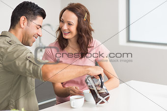 Happy man pouring tea to womans cup in kitchen