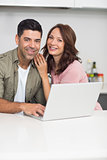 Portrait of a happy couple using laptop in kitchen