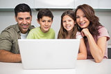 Portrait of a smiling couple with kids using laptop