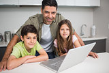 Smiling father with kids using laptop in kitchen