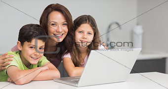 Smiling mother with kids using laptop in kitchen