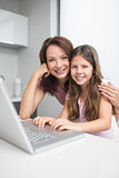 Smiling mother with daughter using laptop in kitchen
