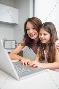 Smiling mother with daughter using laptop in kitchen