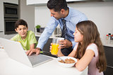 Father using laptop and kids having breakfast in kitchen