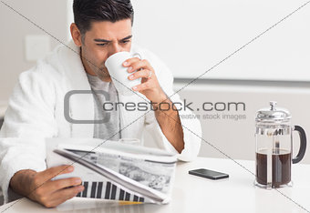 Man drinking coffee while reading newspaper in kitchen