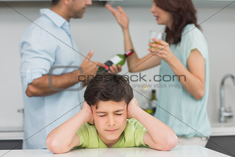 Sad young boy covering ears while parents quarreling