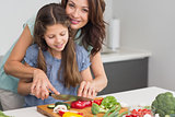 Smiling woman with daughter chopping vegetables in kitchen