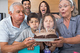Extended family blowing candles on cake in living room