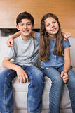 Portrait of smiling little siblings sitting in living room