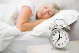 Woman sleeping in bed with alarm clock in foreground at bedroom