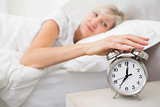 Woman extending hand to alarm clock in bed