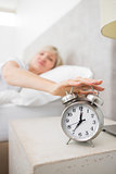 Woman extending hand to alarm clock in bed