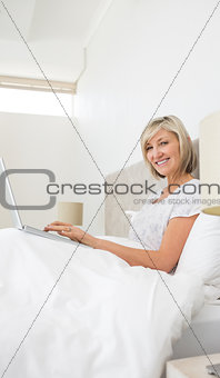 Smiling mature woman using laptop in bed