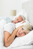 Woman covering ears while man snoring in bed