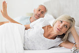 Woman ignoring mature man while lying in bed