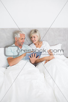 Mature couple using digital tablet in bed