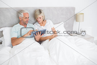 Mature couple using digital tablet in bed