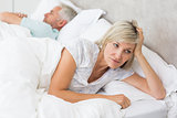 Tensed woman lying besides man in bed